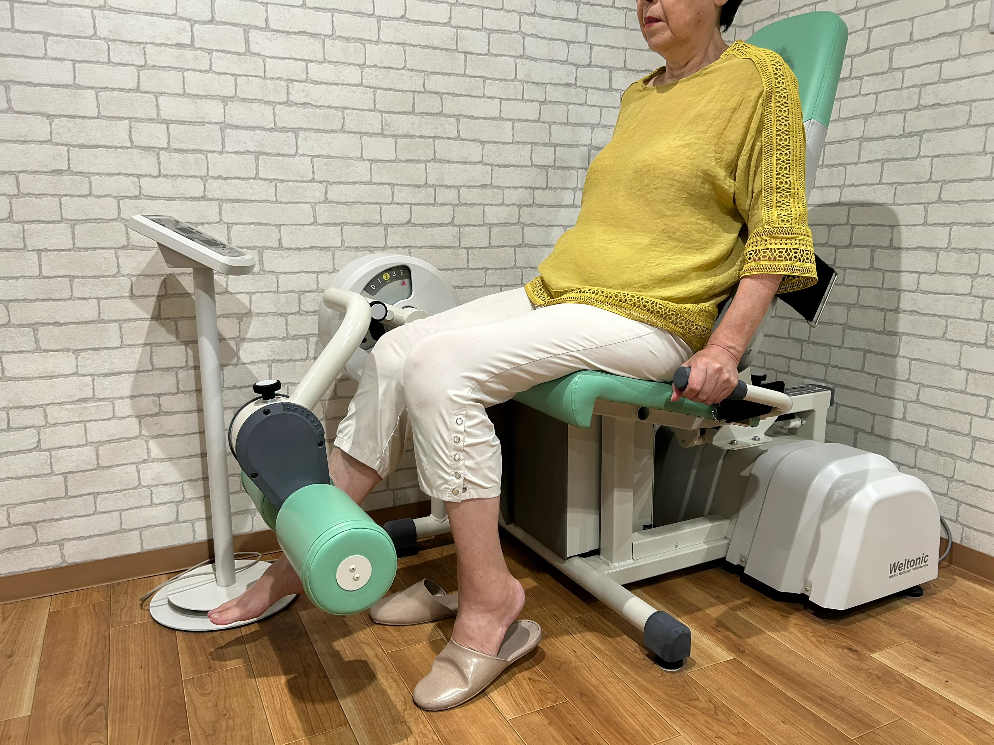 黄色い服の利用者が下肢トレーニング機器で歩く力・立つ力を鍛えている様子